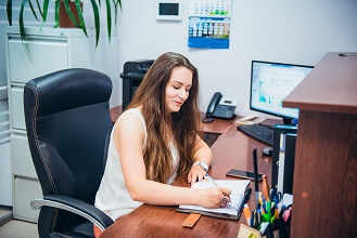 Young caucasian business lady sitting on her workplace in office. Female entrepreneurship. Portrait of skilled manager satisfied with occupation. Selective focus, copy space